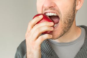 A close up of a man with dental implants biting into a red apple.